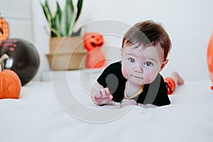 Beautiful baby girl in halloween costume at home, sitting on bed with Halloween decoration, Lifestyle indoors
