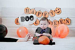Beautiful baby girl with halloween costume at home, sitting on bed with Halloween decoration, mother hand holding BOO sign.