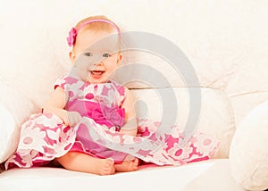 Beautiful baby girl in a pink dress sitting on the couch at home