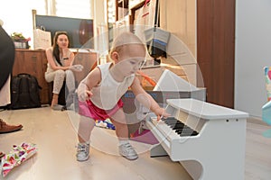 Beautiful baby girl playing toy piano in light room. Authentic image