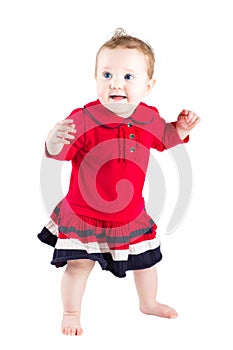 Beautiful baby girl in a red dress making her first steps