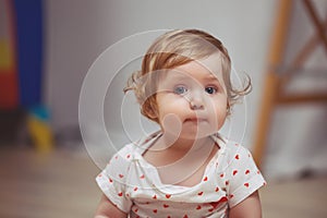 A beautiful baby girl with red hair 10 months plays in the room. The child looks in surprise with big blue