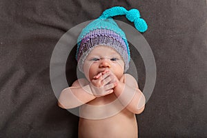 Beautiful baby girl in the studio on a dark gray background in bare pants and a winter hat