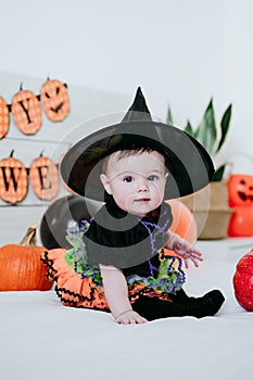 Beautiful baby girl in witch halloween costume at home, sitting on bed with Halloween decoration, Lifestyle indoors