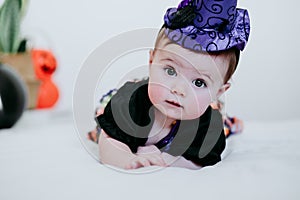 Beautiful baby girl in witch halloween costume at home, sitting on bed with Halloween decoration, Lifestyle indoors