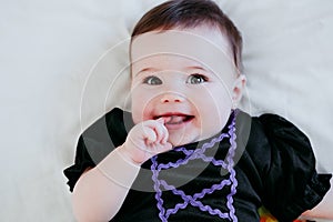 Beautiful baby girl in witch halloween costume at home, sitting on bed with Halloween decoration, Lifestyle indoors