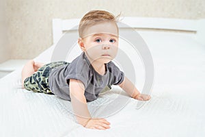 Beautiful baby lying on tummy in parent's bed. Adorable kid crawling on bed in white sunny bedroom.