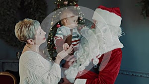 Beautiful baby in mom`s arms and Santa Claus look at each other.