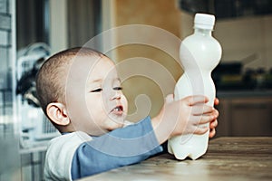 Beautiful baby reaching for milk that is on the table in the plastic bottle