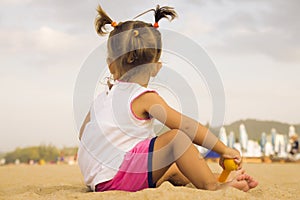 Beautiful baby sitting with his back to the camera and playing with toy rake in the sand on the beach.