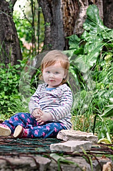 Beautiful baby sitting, smiling and posing, portrait. Little cute girl is playful in garden. Child is playing outside in park.