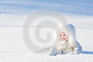 Beautiful baby in a white suit sitting in a snow field