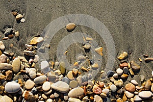 Beautiful background of colorful stones on a sandy wet beach. Sea pebbles, top view