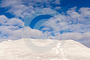 Beautiful background image of snowdrift, a snow hill with tracks from a human, disappearing over the edge. Blue sky and
