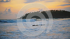 Beautiful background shot of idyllic golden sunset at amazing ocean resort beach and palm island with foamy white waves.