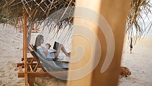 Beautiful background shot of successful female freelancer enjoying drink with laptop in lounge chair on exotic beach.