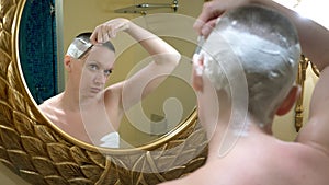 Beautiful bald woman looks in a luxurious bathroom mirror and does her hair, shaves her hair with a dangerous razor
