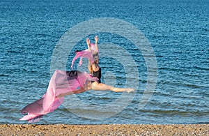 Beautiful ballerina dancing on the shore of the sea in summer time with long dress , sunny day having fun and joy