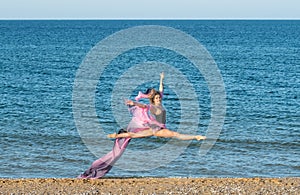 Beautiful ballerina dancing on the shore of the sea in summer time with long dress , sunny day having fun and joy