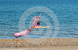 Beautiful ballerina dancing on the shore of the sea in summer time with long dress , sunny day having fun and joy