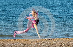 Beautiful ballerina dancing on the shore of the sea in summer time with long dress , sunny day having fun and joy