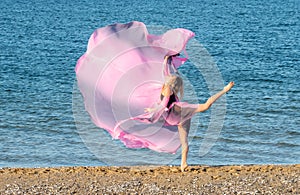 Beautiful ballerina dancing on the shore of the sea in summer time with long dress , sunny day having fun and joy