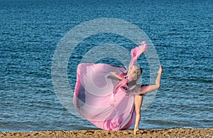 Beautiful ballerina dancing on the shore of the sea in summer time with long dress , sunny day having fun and joy