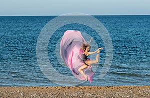 Beautiful ballerina dancing on the shore of the sea in summer time with long dress , sunny day having fun and joy