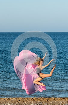 Beautiful ballerina dancing on the shore of the sea in summer time with long dress , sunny day having fun and joy