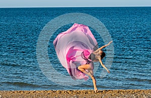 Beautiful ballerina dancing on the shore of the sea in summer time with long dress , sunny day having fun and joy