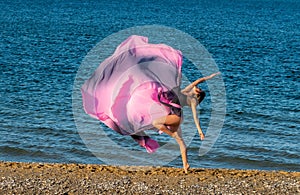 Beautiful ballerina dancing on the shore of the sea in summer time with long dress , sunny day having fun and joy