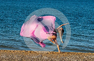 Beautiful ballerina dancing on the shore of the sea in summer time with long dress , sunny day having fun and joy