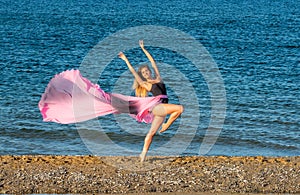 Beautiful ballerina dancing on the shore of the sea in summer time with long dress , sunny day having fun and joy