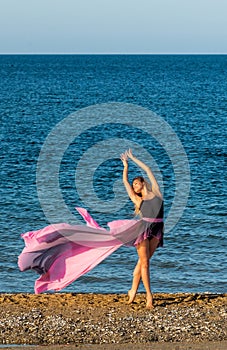 Beautiful ballerina dancing on the shore of the sea in summer time with long dress , sunny day having fun and joy