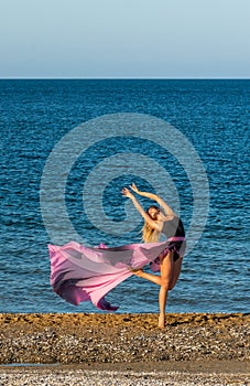 Beautiful ballerina dancing on the shore of the sea in summer time with long dress , sunny day having fun and joy