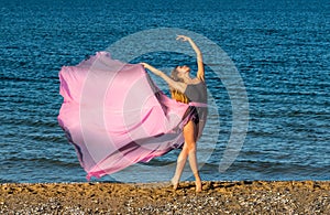 Beautiful ballerina dancing on the shore of the sea in summer time with long dress , sunny day having fun and joy