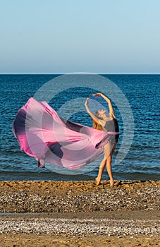 Beautiful ballerina dancing on the shore of the sea in summer time with long dress , sunny day having fun and joy