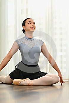 Beautiful ballerina in pointe shoes is sitting on the floor, warming up before dance class