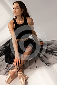 Beautiful ballerina wearing black dress sitting on floor