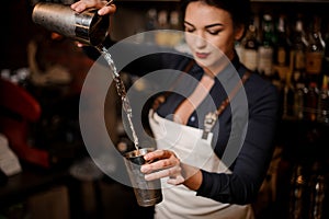 Girl transfusing drink from one steel cocktail shakers to another