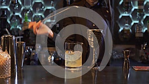 Beautiful bartender young woman with long brown hair mixing cocktail with long spoon in the glass. On the bar is