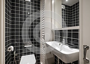 Beautiful bathroom with black glossy square tiles, white ceramic sink with faucet and wooden lockers for towels. The