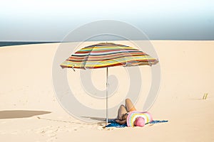 Beautiful beach and caucasian female lay down enjoying a sunbath under a coloured umbrella - concept of summer holiday vacation