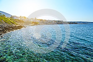 Beautiful beach on coast of Crete with hotels and mountains in background. Rocky shore.