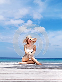 Beautiful beach holiday. Portrait of sexy young woman in white bikini and hat posing by the sea.