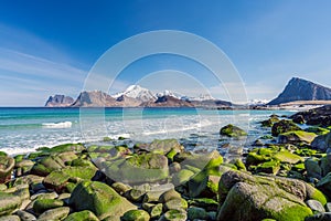 Beautiful beach during springtime on a sunny day with blue sky and silent ocean with small waves and green rocks