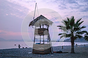 A beautiful beach on a sunset with pink sky. Lifeguard booth near to palm trees. Fethiye, Turkey