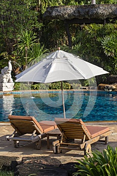 Beautiful beach with swimming pool, palm trees, daybeds and umbrella in a tropical garden near sea