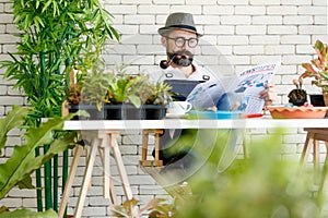 Beautiful beard man wearing hat and eyeglasses and smoking with pipe reading newspaper with wite coffee cup