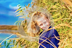 A beautiful, beautiful and young girl in a blue sweater is smiling in the reeds on the bank of the river, her hair backlit by the